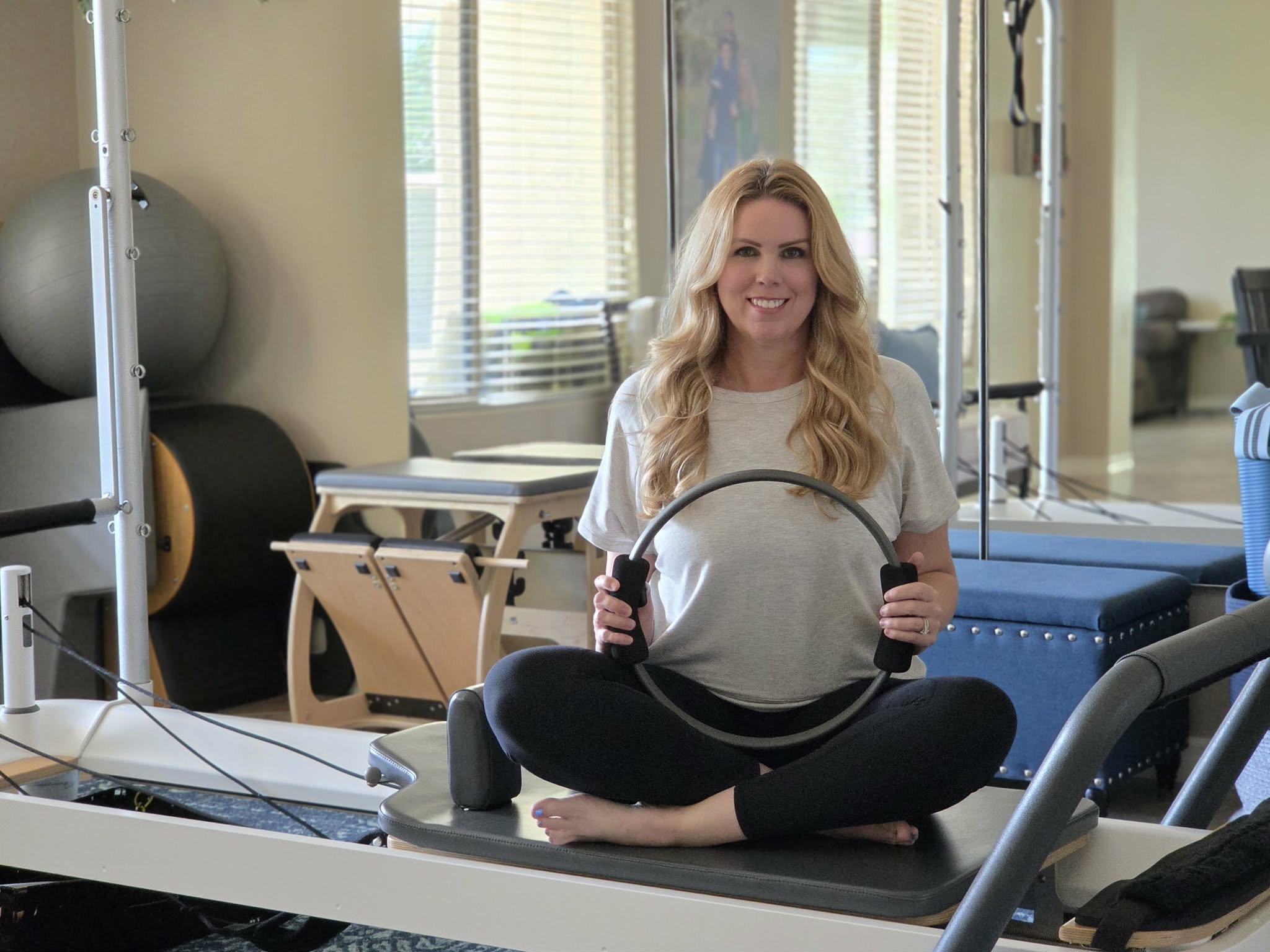 Lindsey seated on a Pilates reformer in her private studio, holding a Pilates ring